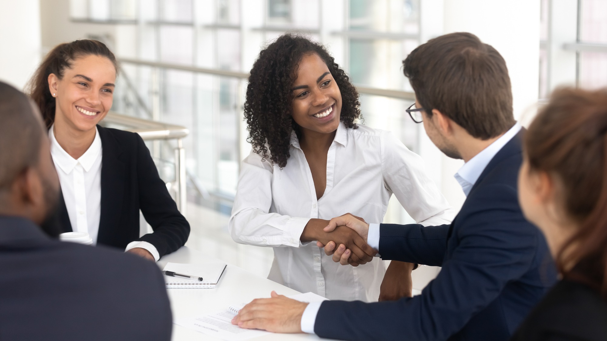 Multiracial businessman businesswoman shake hands starting collaboration at group negotiations, positive people gathered at modern office boardroom, partnership teamwork and business etiquette concept.