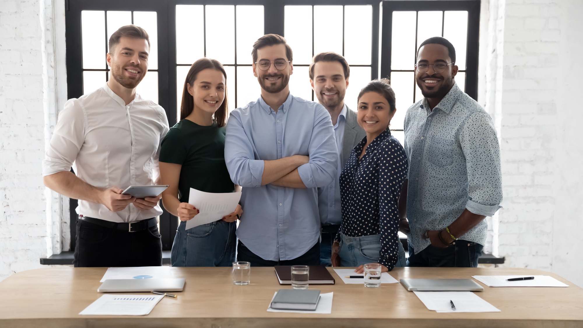 Corporate photo smiling diverse employees with confident executive wearing glasses standing in modern office room, looking at camera, successful startup founder with team, staff members; Shutterstock ID 1792769173; purchase_order: Limited 5/13; job: ; client: ; other: