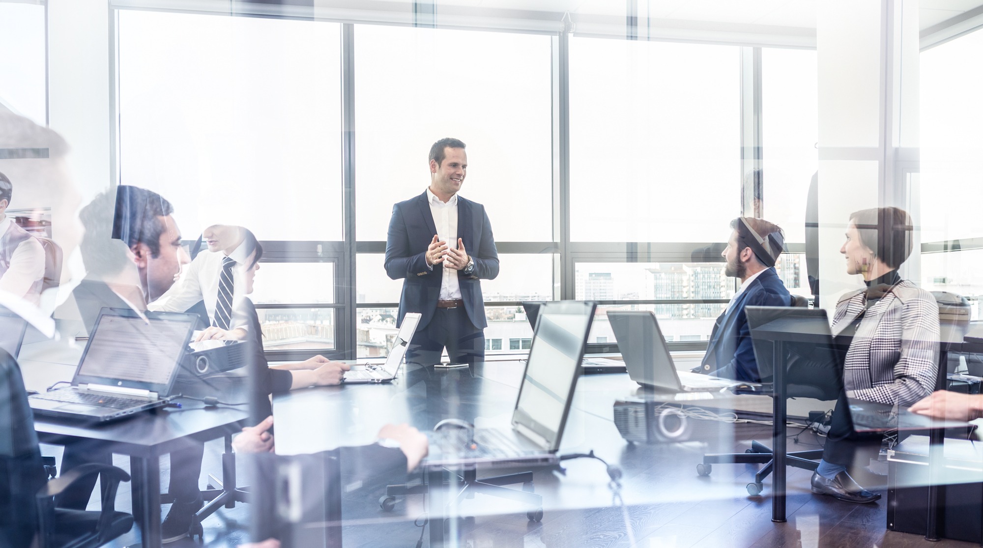 Successful team leader and business owner leading informal in-house business meeting. Businessman working on laptop in foreground. Business and entrepreneurship concept.